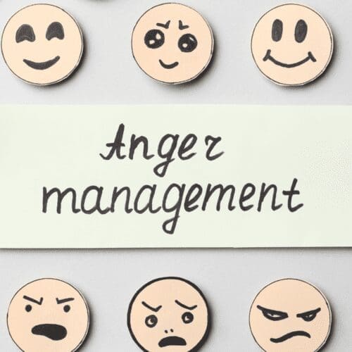 The words Anger Management are written in black cursive on an off-white rectangular area surrounded by different facial expressions on wooden circles on a gray background. Mental Health. Coping Skills. Diversion. Warning Signs. Triggers. Anger Log. Time outs
